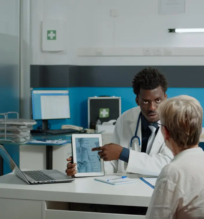 A doctor discusses medical information with a patient in a bright office, surrounded by medical charts and a laptop displaying health data.