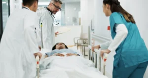 Image of a hospital scene with medical staff surrounding a patient on a stretcher. Image of a hospital scene with medical staff surrounding a patient on a stretcher.
