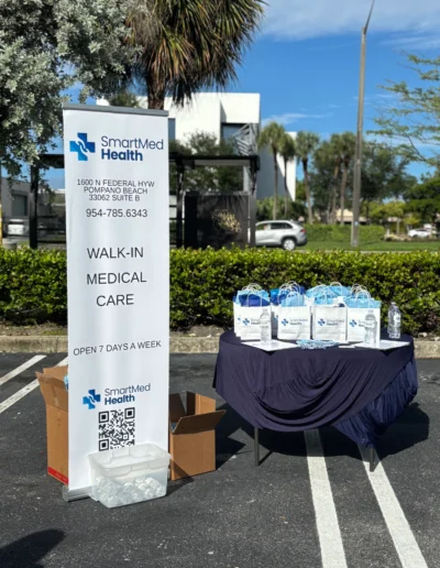 A close-up of a table with promotional items for SmartMed Health. The display includes numerous white gift bags with blue tissue paper, branded water bottles, pens, and informational flyers.